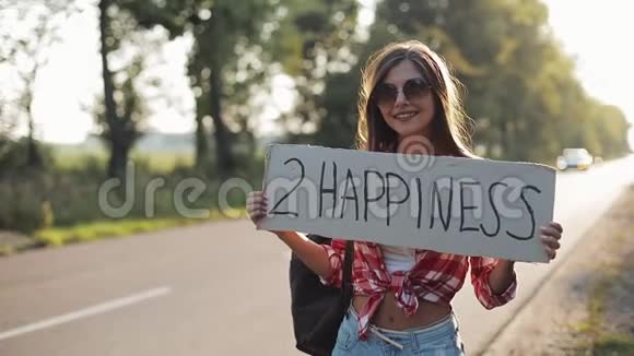 年轻美女搭便车站在路上举着2个幸福的标志夏季视频的预览图