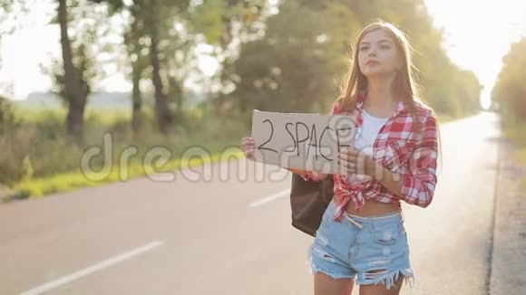 年轻美女搭便车站在路上举着2个空间标志夏季视频的预览图