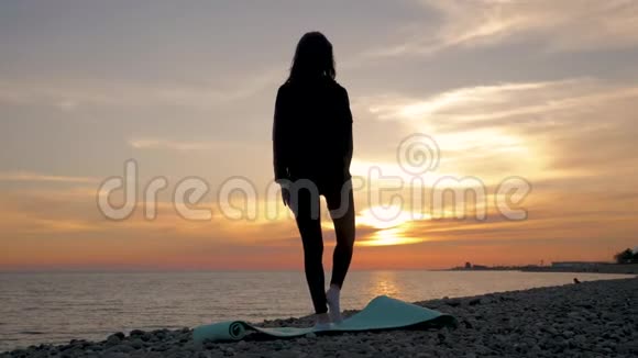 剪影年轻女子在海上日落时练习瑜伽快乐的生活时刻海滩上的剪影瑜伽视频的预览图