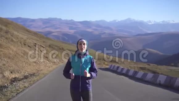 一个身穿头巾的穆斯林运动女子在背景山上阳光明媚的道路上奔跑的肖像视频的预览图