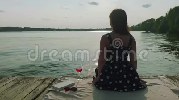 坐在老码头上的幸福女人的后景女人看着前方喝了一杯红酒然后放进去视频的预览图