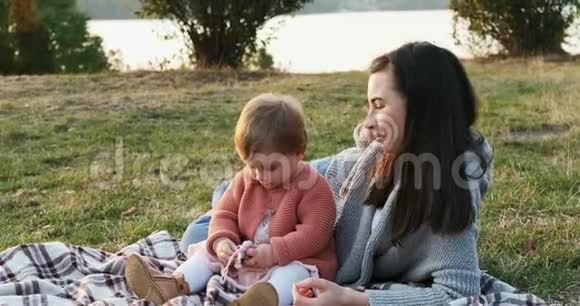 母亲和一个小女儿一起在城市公园野餐年轻的女人和小女孩在玩视频的预览图