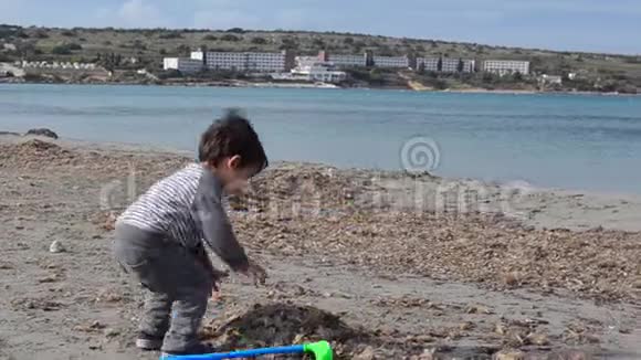 可爱的幼儿在沙滩上玩塑料高尔夫球棒和沙滩海藻视频的预览图