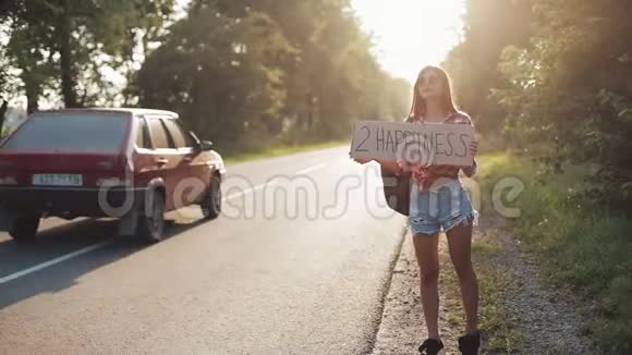 年轻美女搭便车站在路上举着2个幸福的标志夏季视频的预览图