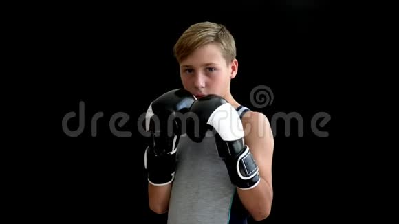 一个金发棕色眼睛的拳击男孩站在黑暗的背景上拳击手十几岁的人双手戴手套他视频的预览图