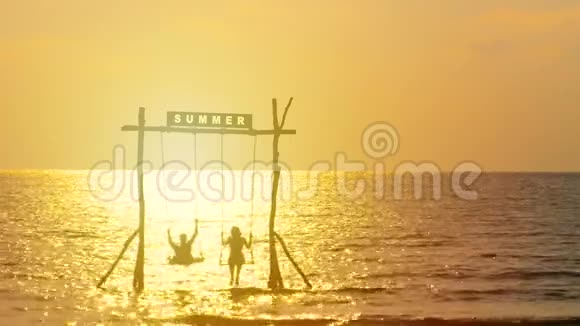 4K幸福夫妇的剪影喜欢在日落时间随着秋千在海上摇曳夏天的标志在上面视频的预览图