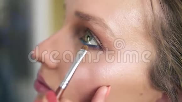 模特脸侧视化妆师用刷子在下眼睑下涂抹眼影蓝色眼线制作视频的预览图