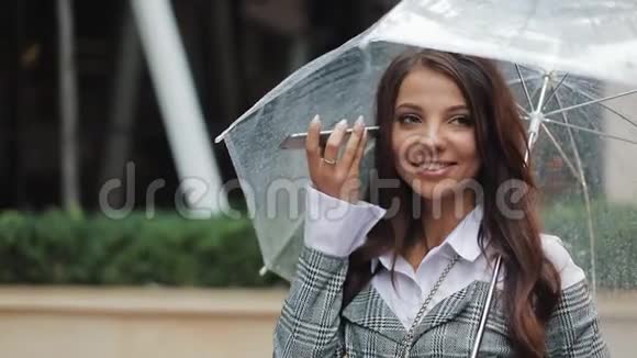 商务女性戴着黑色帽子手里拿着雨伞在户外用手机发送语音信息视频的预览图