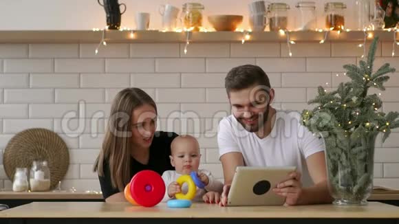 母亲父亲和婴儿的家人坐在家里带着平板电脑视频的预览图