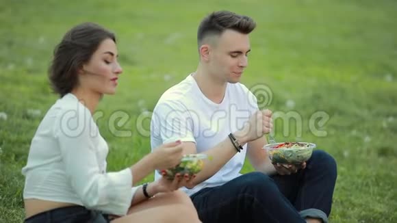 年轻夫妇坐在草地上吃沙拉一起野餐视频的预览图