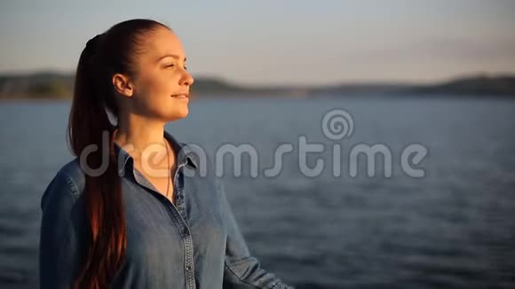 傍晚时分一位白发苍苍的年轻女子站在河边的河堤上举起她的头发视频的预览图