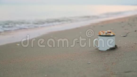 近景金属白色杯子里面装满了贝壳站在沙质海岸上靠近景模糊的雄性腿沿海岸奔跑视频的预览图