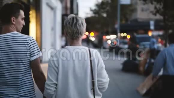幸福的年轻浪漫夫妇牵着手走在傍晚的索霍纽约模糊的路灯背景视频的预览图