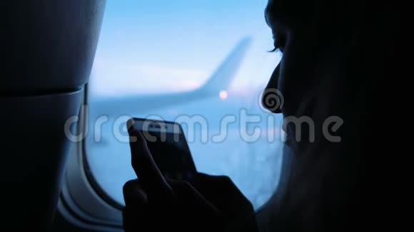 日落时分女人在飞机窗口附近使用智能手机特写镜头视频的预览图