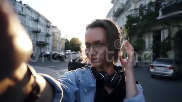 一个戴眼镜的年轻女孩摆姿势伸出的手上戴着照相机微笑快乐显示一个手势酷视频的预览图
