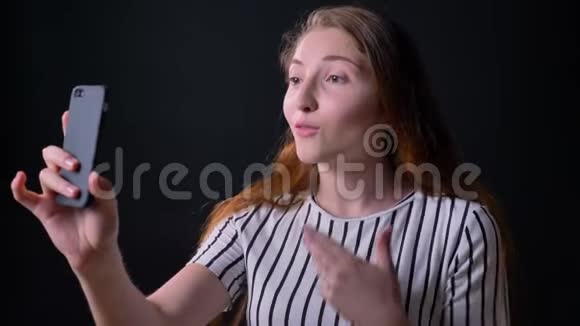 一位迷人的年轻女子长着姜黄色的头发通过电话和笑声进行视频聊天她孤独地站在黑色的床上视频的预览图