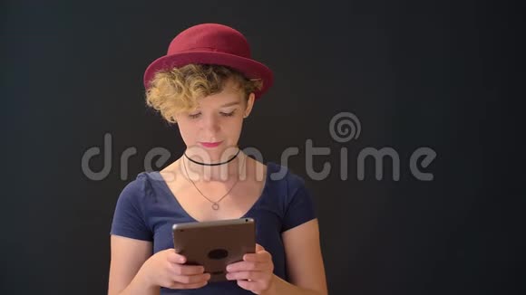 一位留着红色帽子的卷发的年轻女子在平板电脑上打字被隔离在黑色背景上视频的预览图