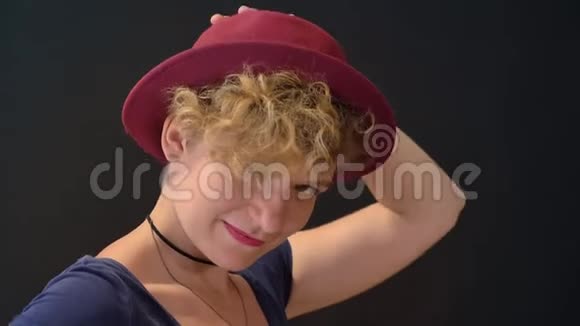 可爱的年轻女人一头卷曲的金发戴着帽子微笑着被孤立在黑色的背景上视频的预览图
