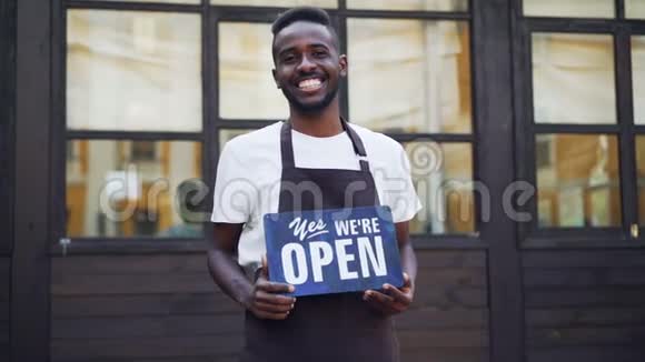 慢镜头肖像欢快的非裔美国人商人咖啡馆老板举着我们的开放标志站在外面视频的预览图