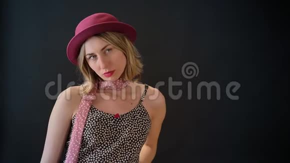 年轻的金发女郎戴着粉红色的帽子摆姿势拍照站在黑人工作室的背景上视频的预览图