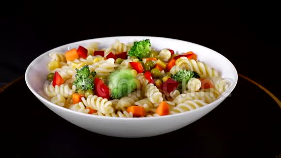 盘子上有蔬菜的螺旋面在黑色背景上旋转绿色油菜花落在盘子里视频的预览图