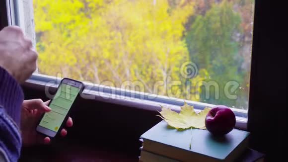 秋天男人滚动智能手机在窗前搅拌一杯茶视频的预览图