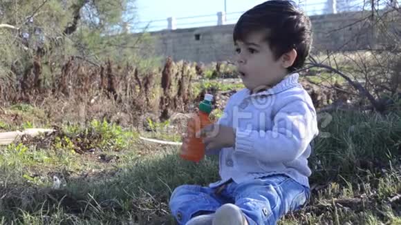 可爱的两岁男孩从大自然的瓶子里喝水视频的预览图