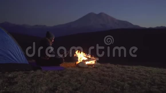 夜晚的女游客坐在帐篷旁手牵着火群山是可见的慢悠悠的视频的预览图