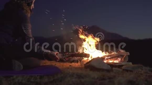 年轻的野营妇女坐着把木头扔进燃烧的火里慢悠悠视频的预览图