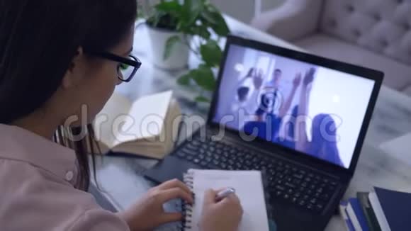 电子培训戴眼镜的女生在笔记本上看视频时用钢笔在笔记本上写字视频的预览图