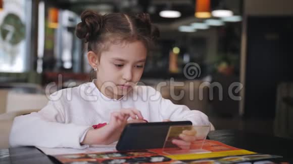 小女孩在智能手机上玩游戏在网上坐在咖啡馆的桌子旁视频的预览图