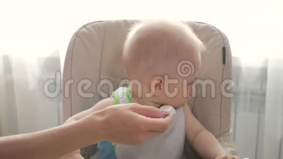 婴儿坐在孩子们小桌子旁妈妈给孩子喂粥妈妈用勺子给婴儿食物视频的预览图