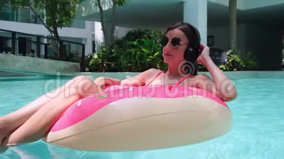 快乐的女人和充气的游泳圈在游泳池里的甜甜圈形状在商店里听音乐视频的预览图