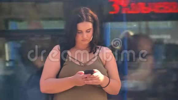 美丽的年轻黑发女人肥胖的发短信对着镜头微笑站在站台上火车在视频的预览图