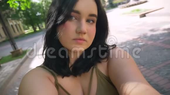 美丽肥胖的年轻女子在网络摄像机上录制视频微笑着站在大学附近公园的街道上视频的预览图