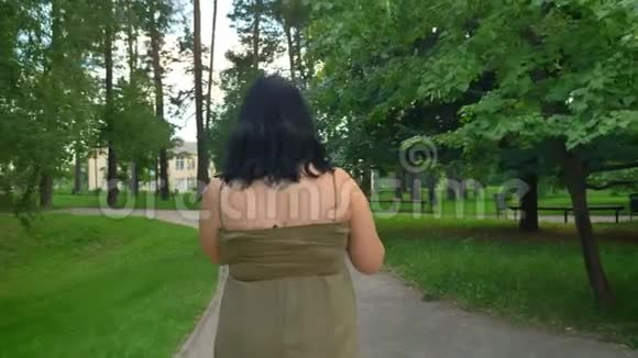 美丽的年轻肥胖女人的后景自拍和步行公园与树木和绿草迷人的女士在视频的预览图