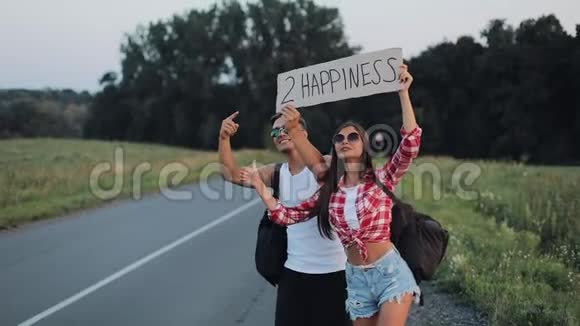 一对年轻夫妇正站在路上搭便车一男一女在高速公路上用一个标志停车视频的预览图