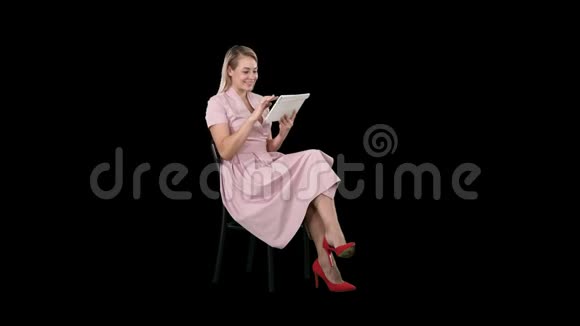 有趣的漂亮年轻女子穿着粉色连衣裙坐在椅子上用平板电脑阿尔法频道视频的预览图