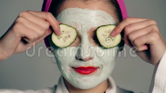 一个女孩头上戴着面罩和毛巾用灰色背景的黄瓜闭上眼睛视频的预览图