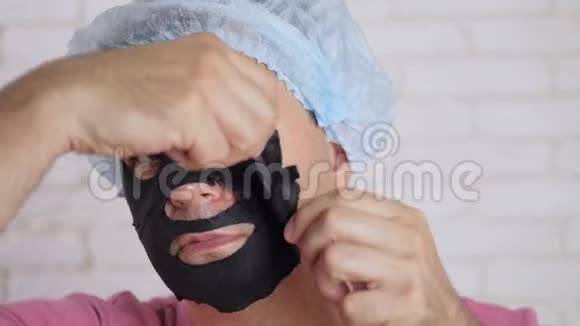 一个男人从他的脸上摘下一个恢复活力的黑色化妆面具微笑着看着镜子视频的预览图
