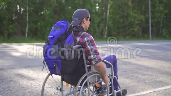 残疾人坐轮椅背着背包在高速公路上旅行后景慢节奏视频的预览图