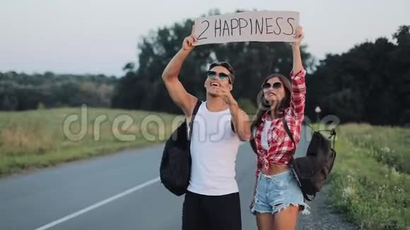 年轻的旅行情侣相爱站在路上举着一个标志2幸福快乐的微笑的朋友们正在关注视频的预览图