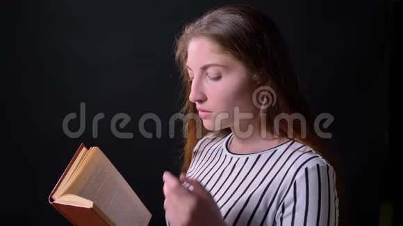 美丽动人的年轻女子阅读书籍和思考侧写观在黑色背景上孤立视频的预览图