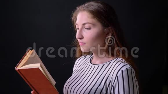 年轻漂亮的女人看书孤零零地站在黑色背景上侧影视频的预览图