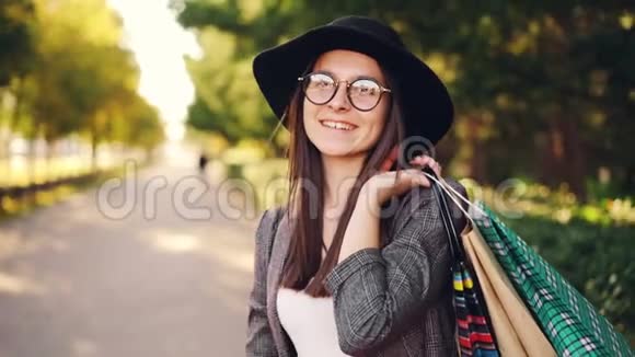 快乐年轻的黑发小姐站在户外看着相机微笑着手里拿着购物袋视频的预览图