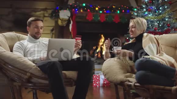 丈夫使用笔记本电脑和信用卡上网购物而妻子则在圣诞节晚上喝咖啡视频的预览图