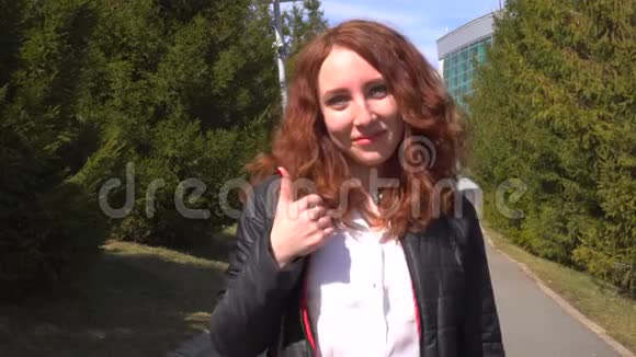 年轻漂亮的红发女孩在户外街头散步在公园里竖起大拇指视频的预览图