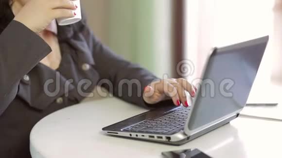 一个女人从一次性杯子里喝一杯饮料在笔记本电脑上工作慢节奏视频的预览图