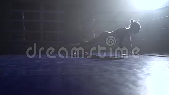 女人在黑暗的拳击场里从地板上挤下来剪影慢动作视频的预览图
