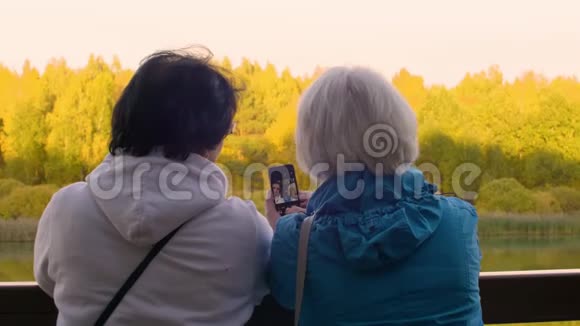 两位老人在户外河边的栏杆旁打电话自拍视频的预览图